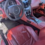 アストンマーチン DB9の運転席コックピット全体を見下ろしたアングル。鮮やかな本革赤レザーシートとマンソリー仕様の内装パネル。Mガレージ福岡で販売中の上質なカスタム金融車。